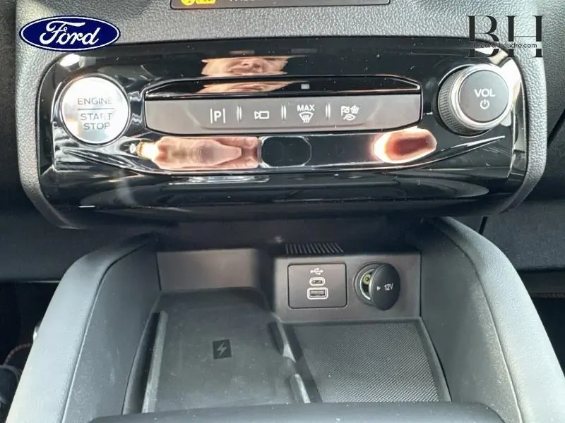 Vue rapprochée de la console centrale noire brillante du Ford Kuga 2025 avec bouton start/stop et ports USB et 12V.