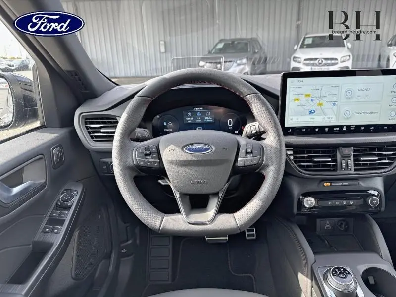 Vue intérieure centrée sur le volant sport du Ford Kuga gris, avec tableau de bord digital et écran tactile GPS.