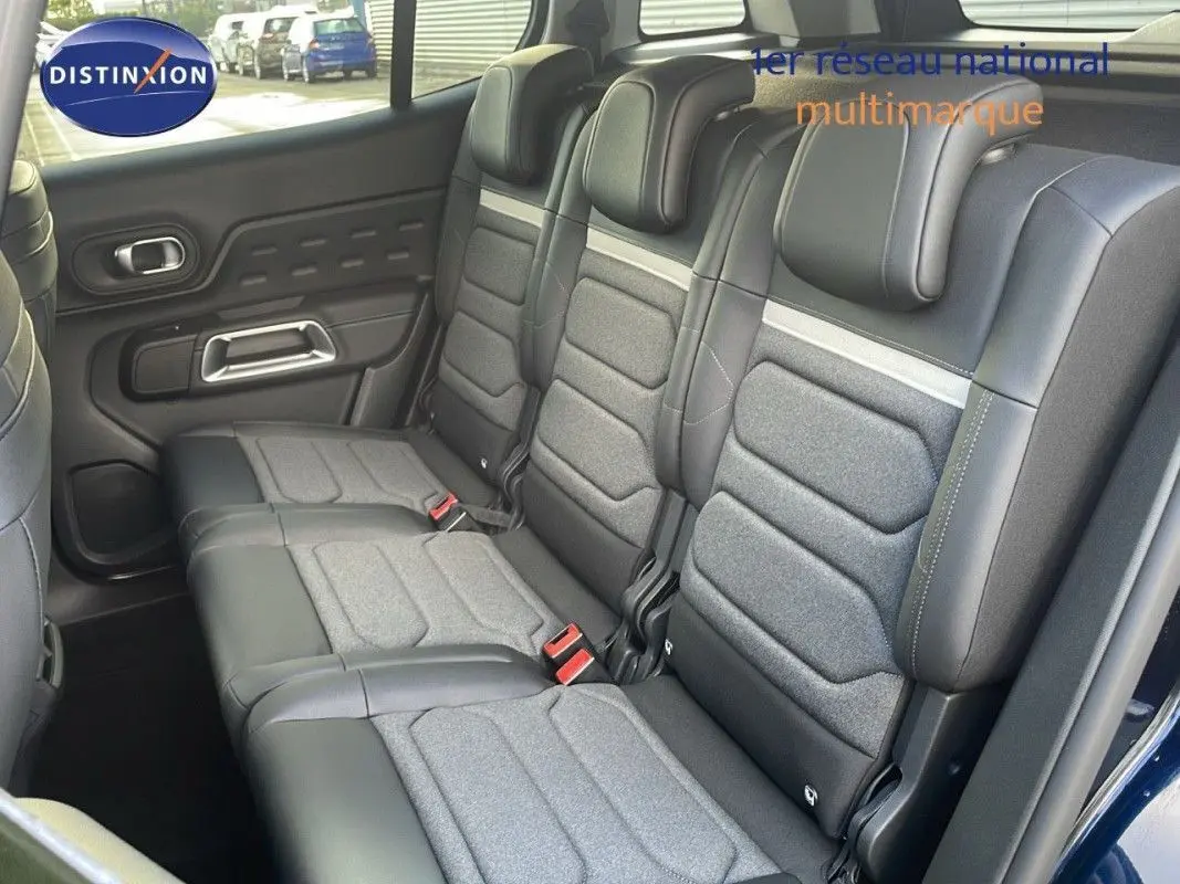 Vue intérieure arrière du Citroën C5 Aircross 2025 montrant les sièges en tissu gris et cuir noir avec ceintures rouges.