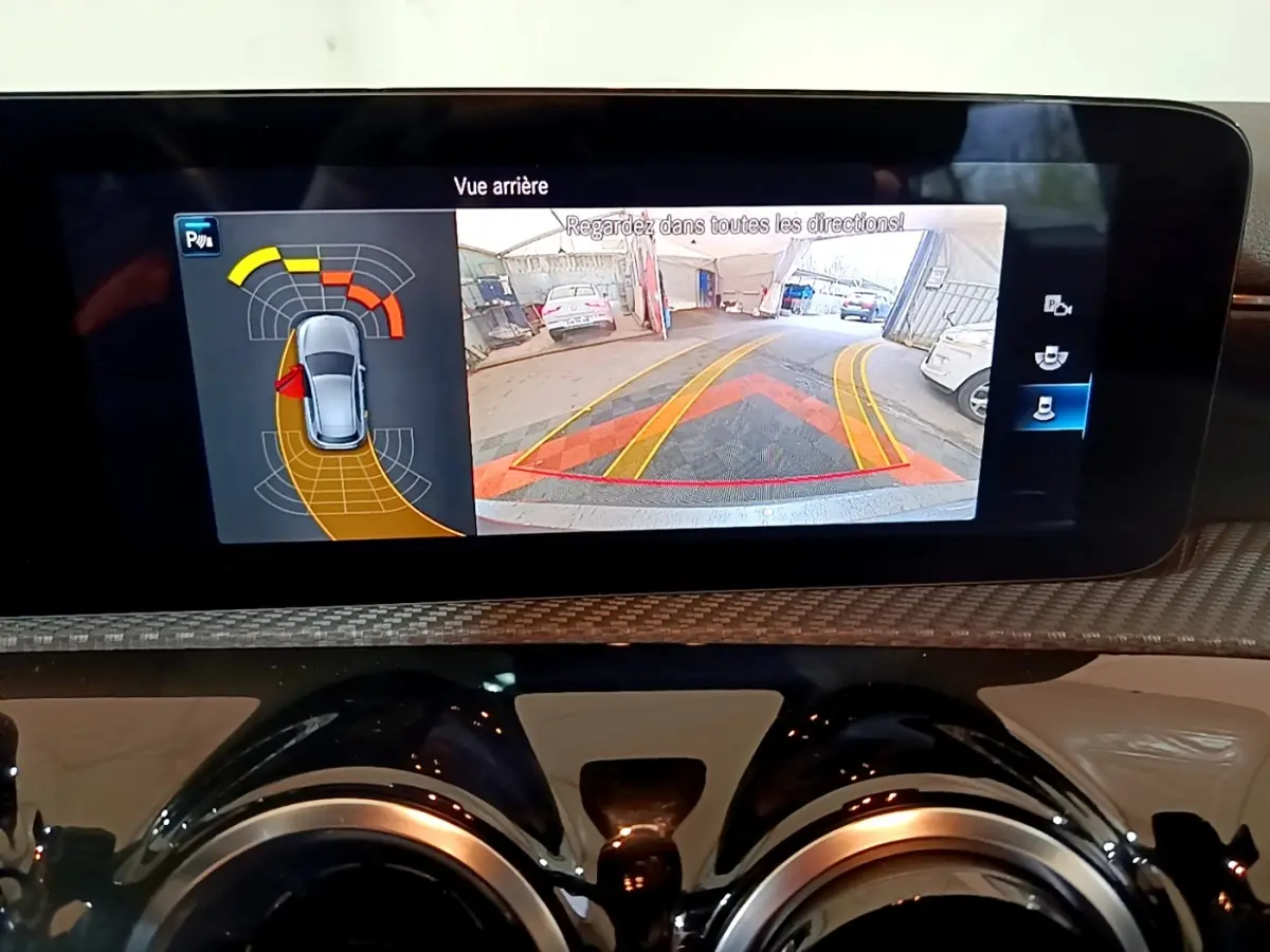 Écran tactile intérieur montrant l’aide au stationnement arrière avec vue caméra et capteurs sur Mercedes Classe A gris foncé.