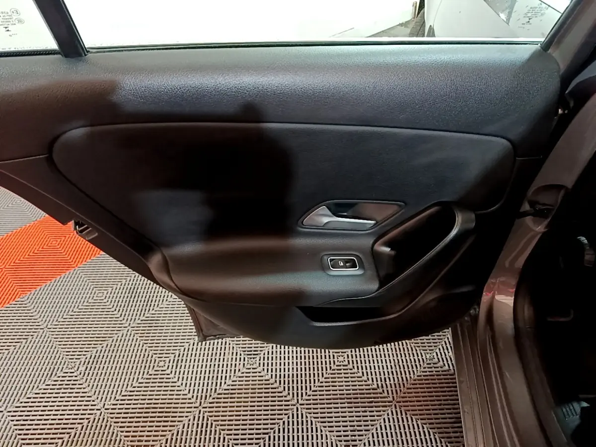 Vue intérieure de la porte arrière droite d'une Mercedes Classe A gris foncé, avec poignée argentée et bouton de vitre électrique.