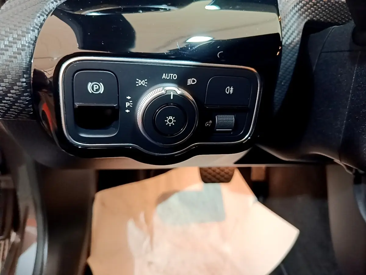 Gros plan sur le panneau de commande des phares et du frein à main électrique dans une Mercedes Classe A gris foncé.