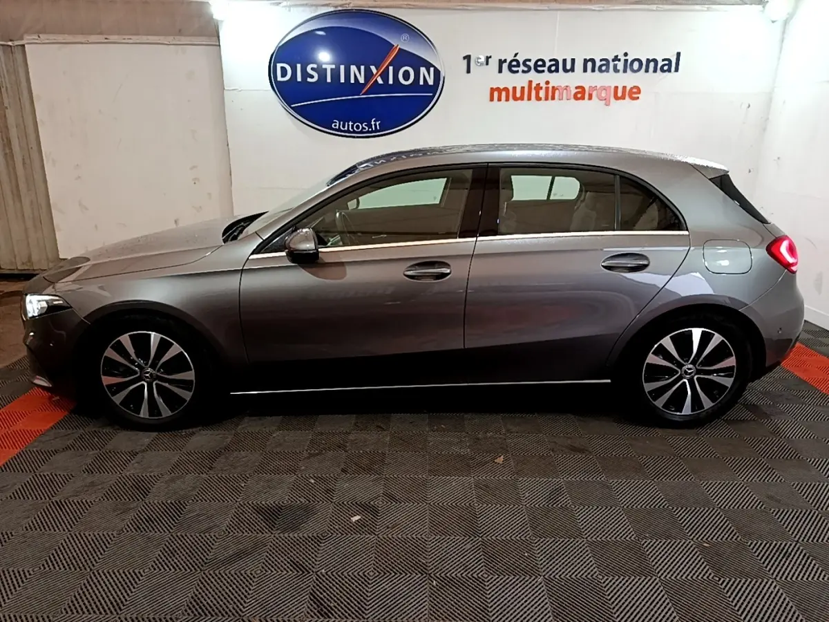 Vue de profil côté gauche d'une Mercedes Classe A 180 d Business Line gris foncé avec jantes alliage et feux arrière allumés.