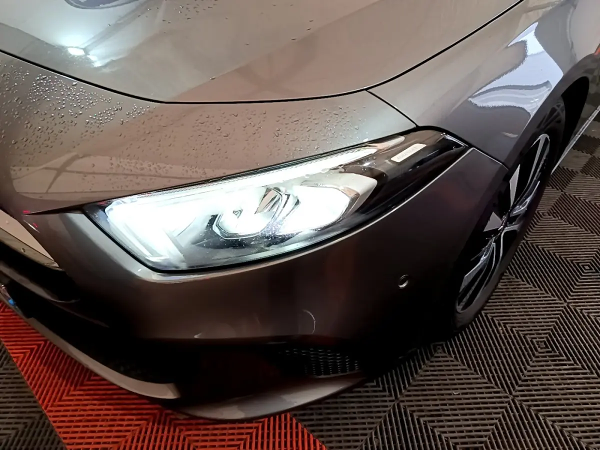 Gros plan sur l'avant droit gris foncé d'une Mercedes Classe A 180 d avec phare LED allumé et jante visible.