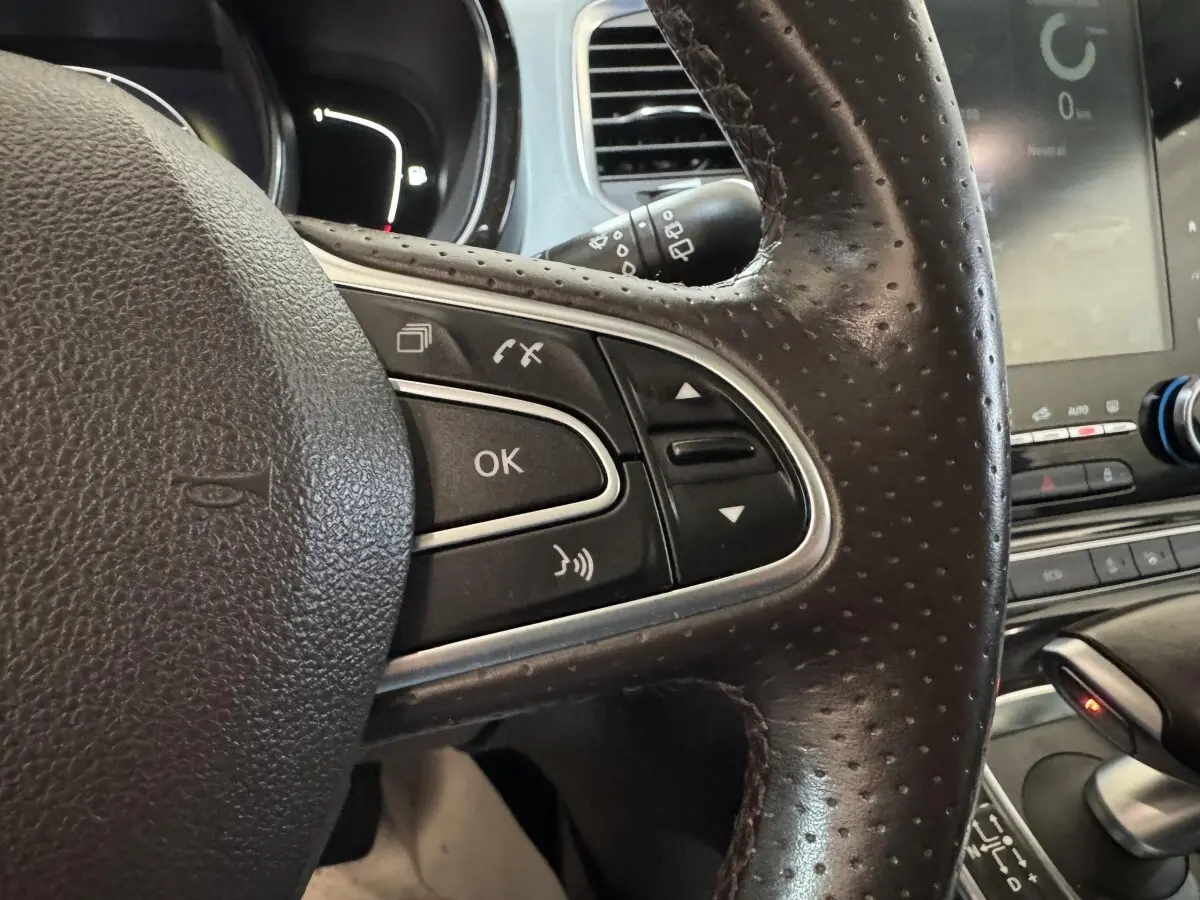 Gros plan sur le volant en cuir noir perforé côté gauche du Renault Espace gris foncé avec commandes multifonctions et écran tactile visible.