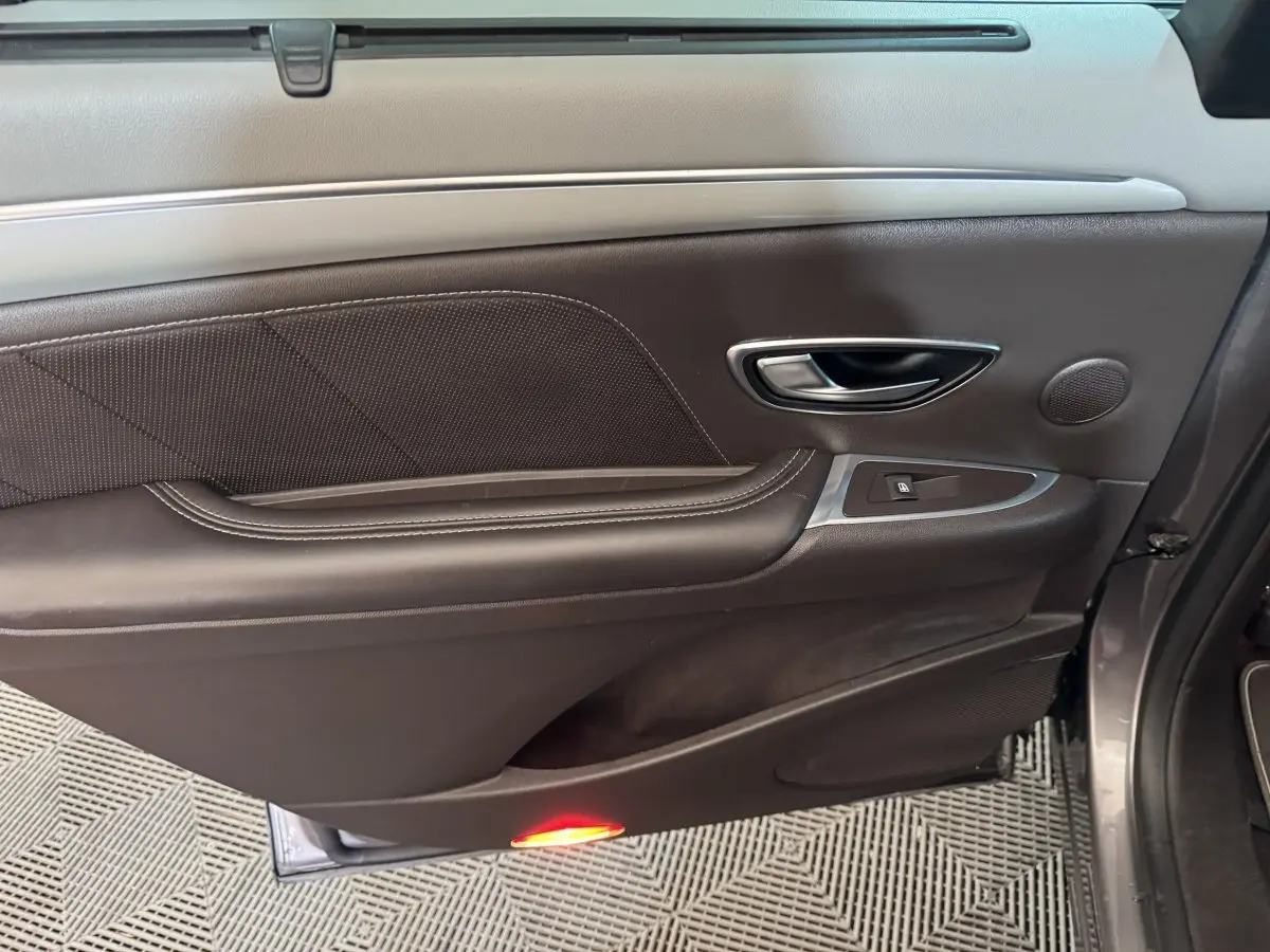 Vue côté gauche de la porte intérieure en cuir noir avec poignée alu et éclairage de seuil rouge du Renault Espace gris foncé 2015.