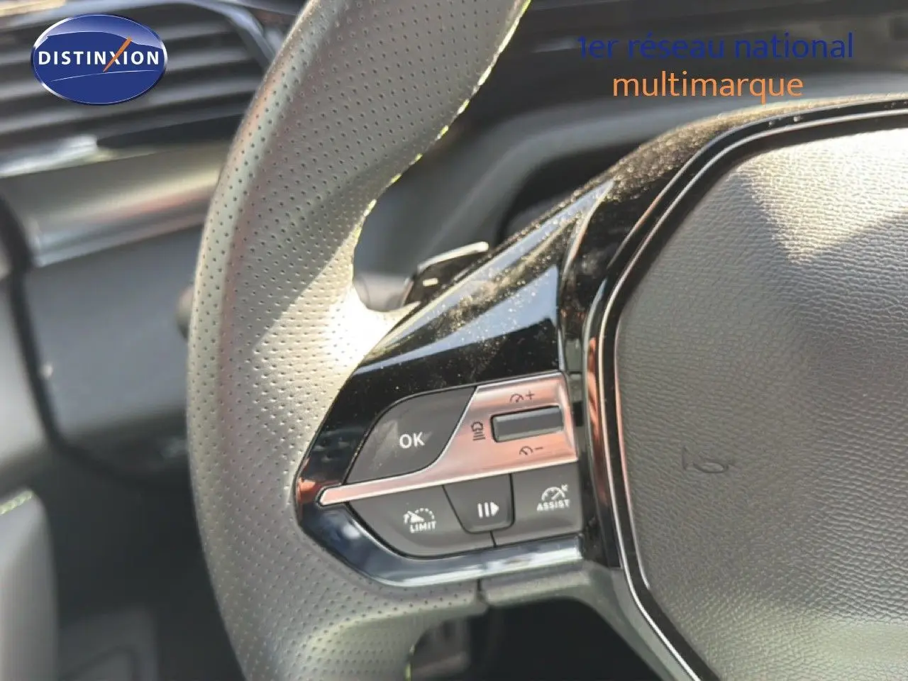 Gros plan sur le volant cuir perforé de la Peugeot 408 1.2 Hybrid 2025 avec commandes intégrées côté gauche.