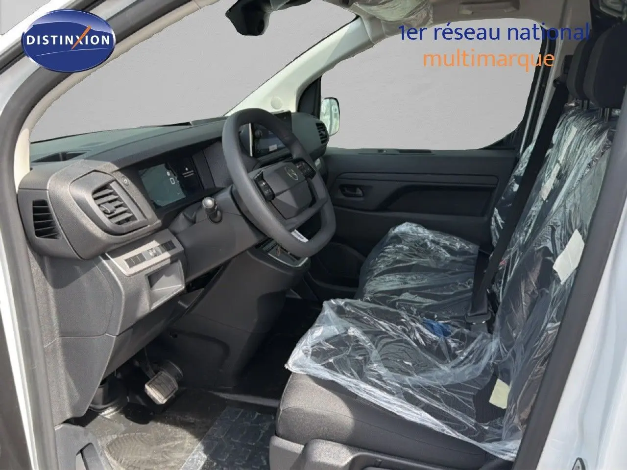 Intérieur côté conducteur du Citroën Jumpy blanc Kaolin, sièges avant protégés par film plastique, tableau de bord moderne noir.