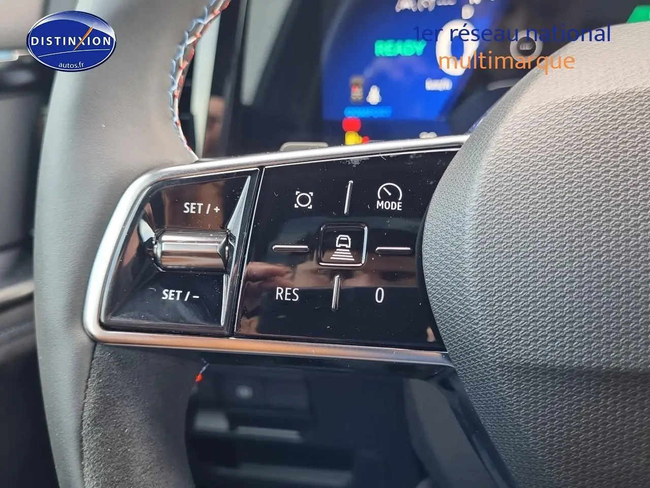 Gros plan sur les commandes du volant gris du Renault Espace VI hybride, avec affichage numérique flou en arrière-plan.