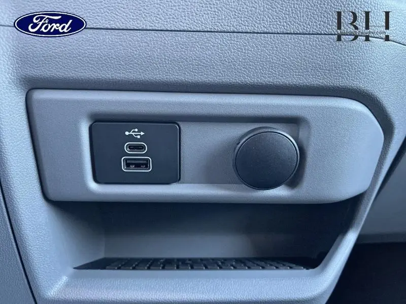 Gros plan sur les ports USB et prise 12V intégrés dans la console grise du Ford Transit Custom Fourgon 2025