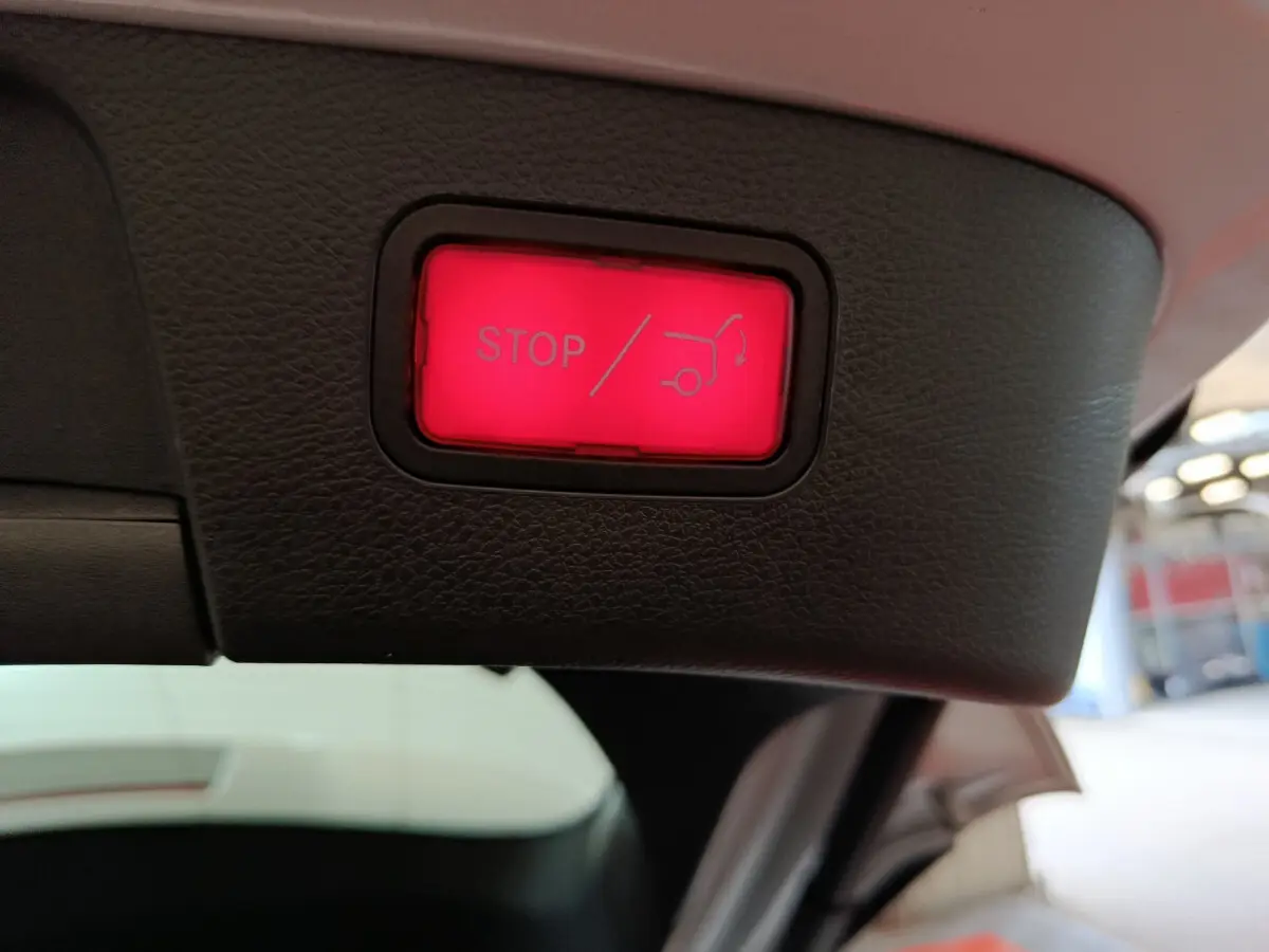 Bouton rouge d'arrêt électrique du coffre sur le hayon intérieur d'un Mercedes GLA gris clair, vue rapprochée.