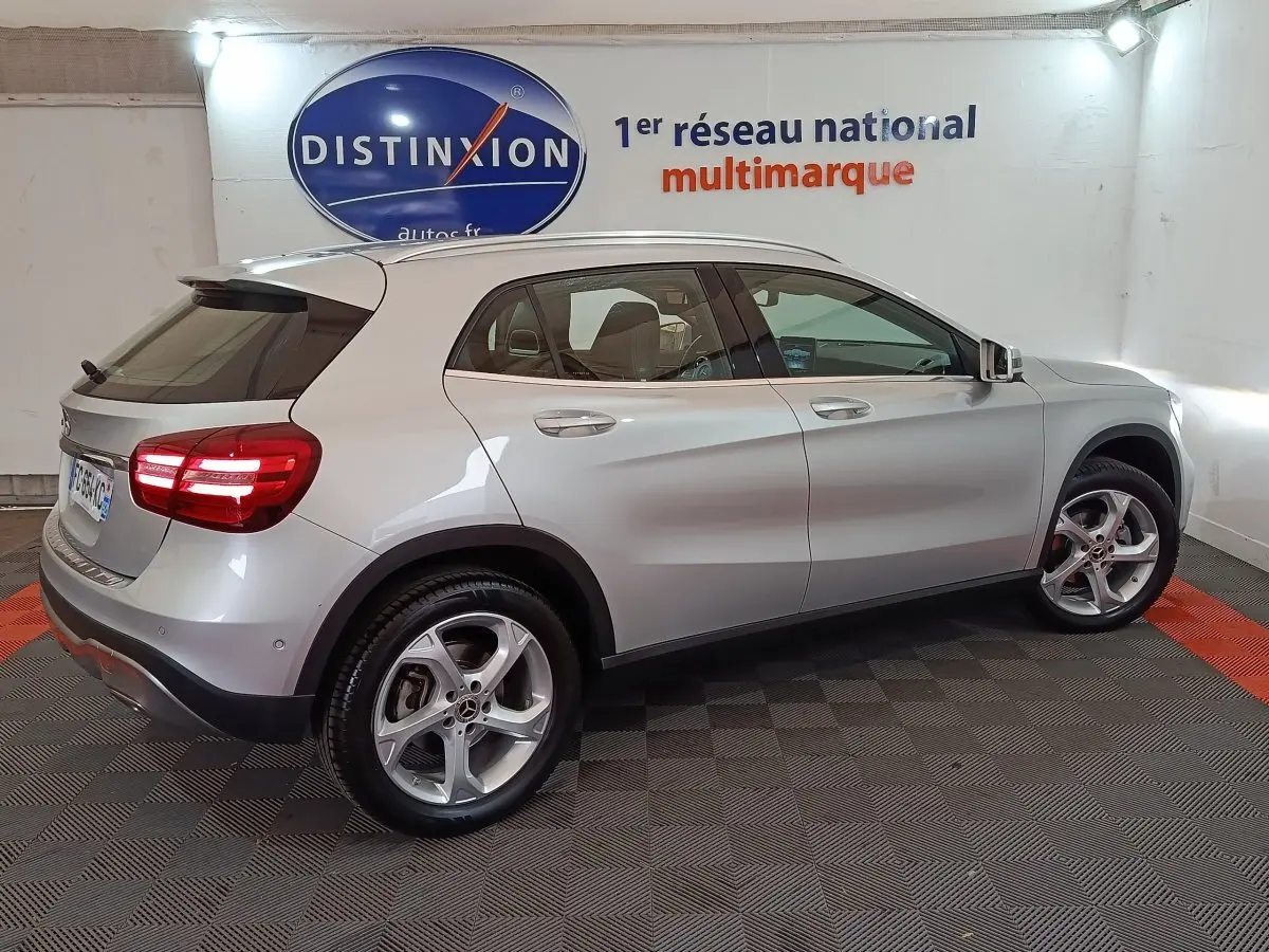 Vue côté droit arrière d'un Mercedes GLA 200 d gris clair avec jantes alliage et feux arrière LED allumés en intérieur showroom.