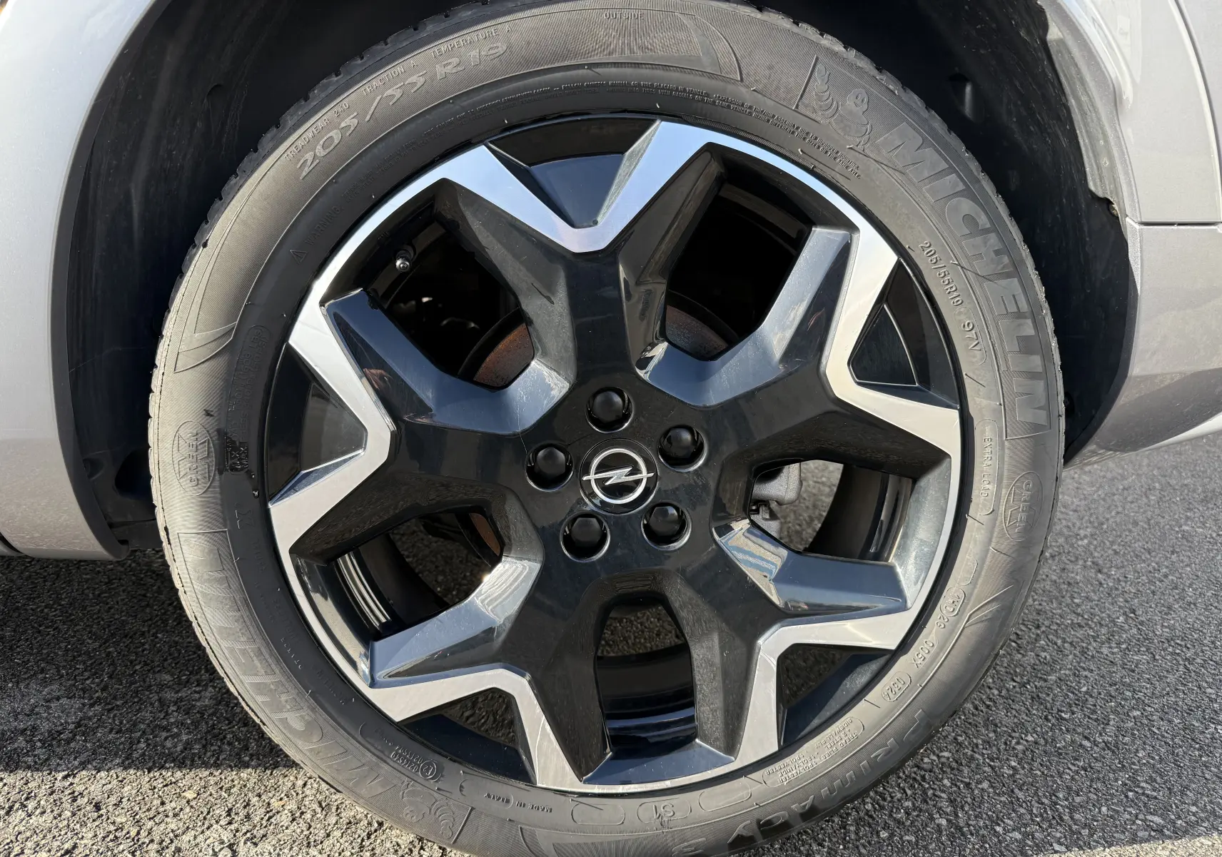 Gros plan sur la roue avant gauche de l'Opel Grandland gris Artense avec jante alliage noire et argentée.