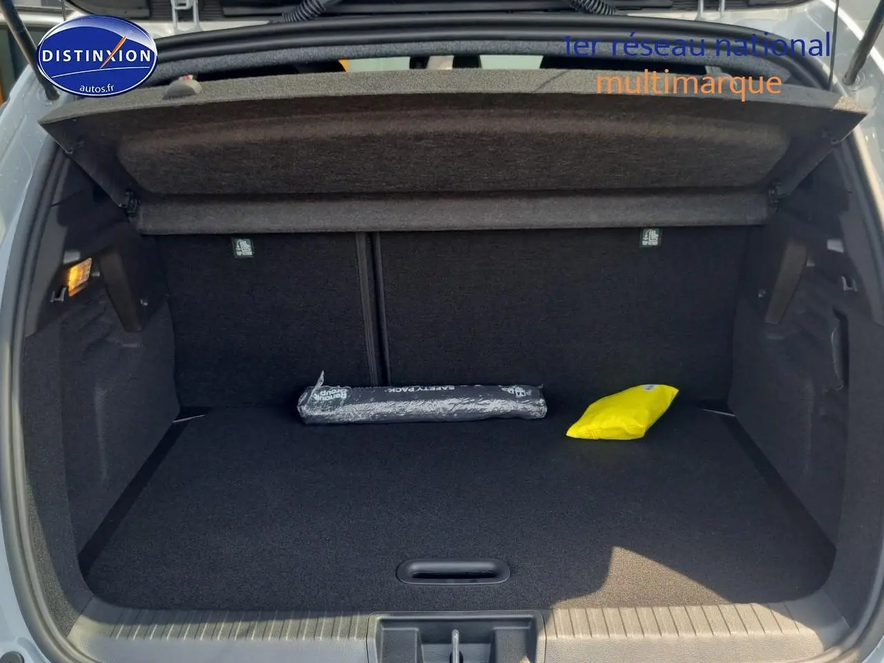 Coffre ouvert d'un Renault Captur gris rafale, montrant un espace de rangement avec tapis noir et deux accessoires.