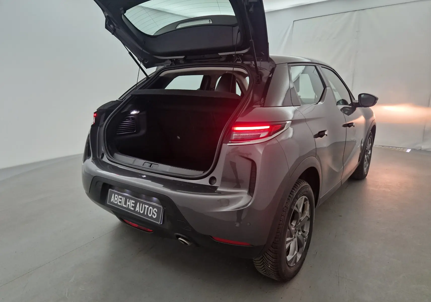 Vue 3/4 arrière droite d'un DS3 Crossback gris platinium avec coffre ouvert et feux arrière allumés dans un studio.