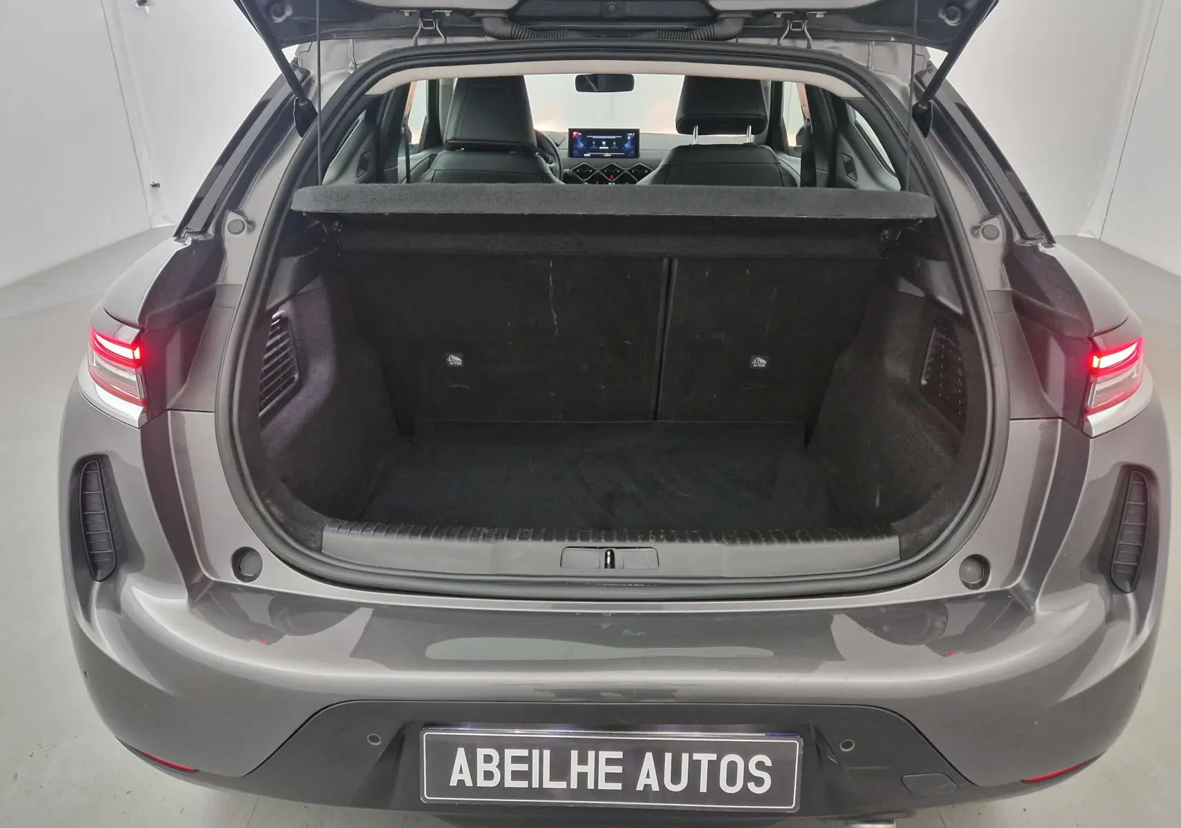 Vue arrière ouverte du coffre d'un DS3 Crossback gris platinium 2022 avec feux arrière allumés dans un studio blanc.