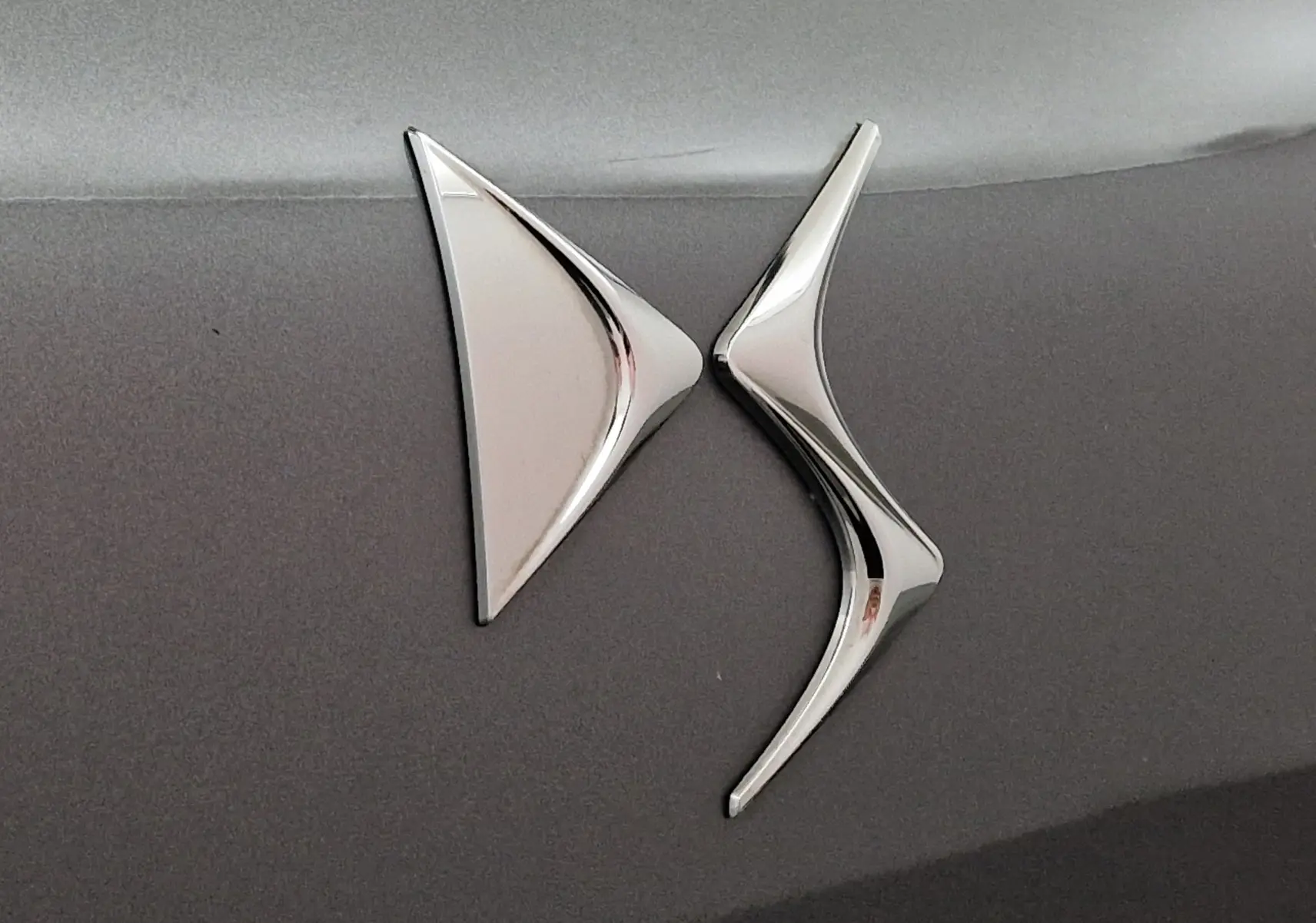 Gros plan sur le logo chromé DS sur la carrosserie gris platinium du DS3 Crossback 2022.