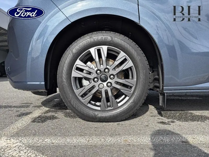 Gros plan sur la roue avant gauche du Ford Transit Custom bleu azur métallisé avec jante alu gris carbone à 6 branches.