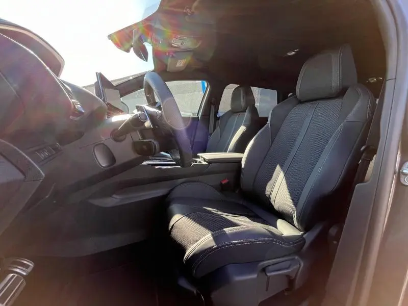 Intérieur avant du Peugeot 5008 gris, sièges tissu noir avec surpiqûres blanches et volant multifonction visible de profil droit.