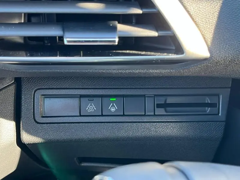 Détail du tableau de bord gris du Peugeot 5008 2024 montrant les boutons d'aide à la conduite avec témoin vert allumé.