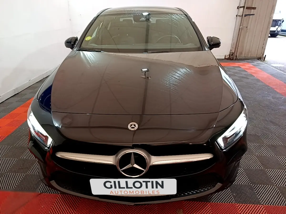Vue avant d'une Mercedes Classe A berline noire avec calandre chromée et phares LED allumés dans un garage.