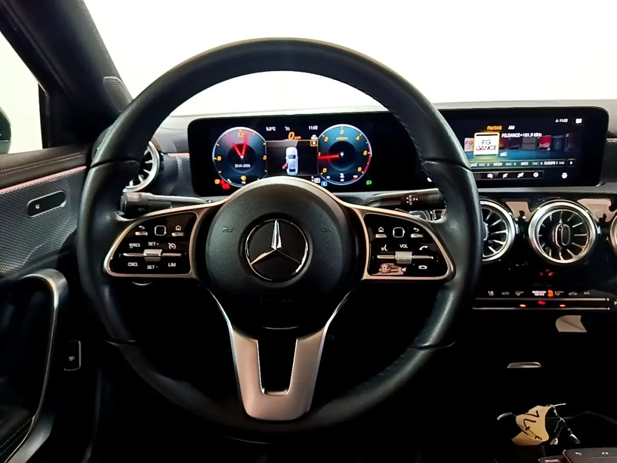 Vue intérieure centrée sur le volant cuir noir et le tableau de bord numérique de la Mercedes Classe A berline 2022.
