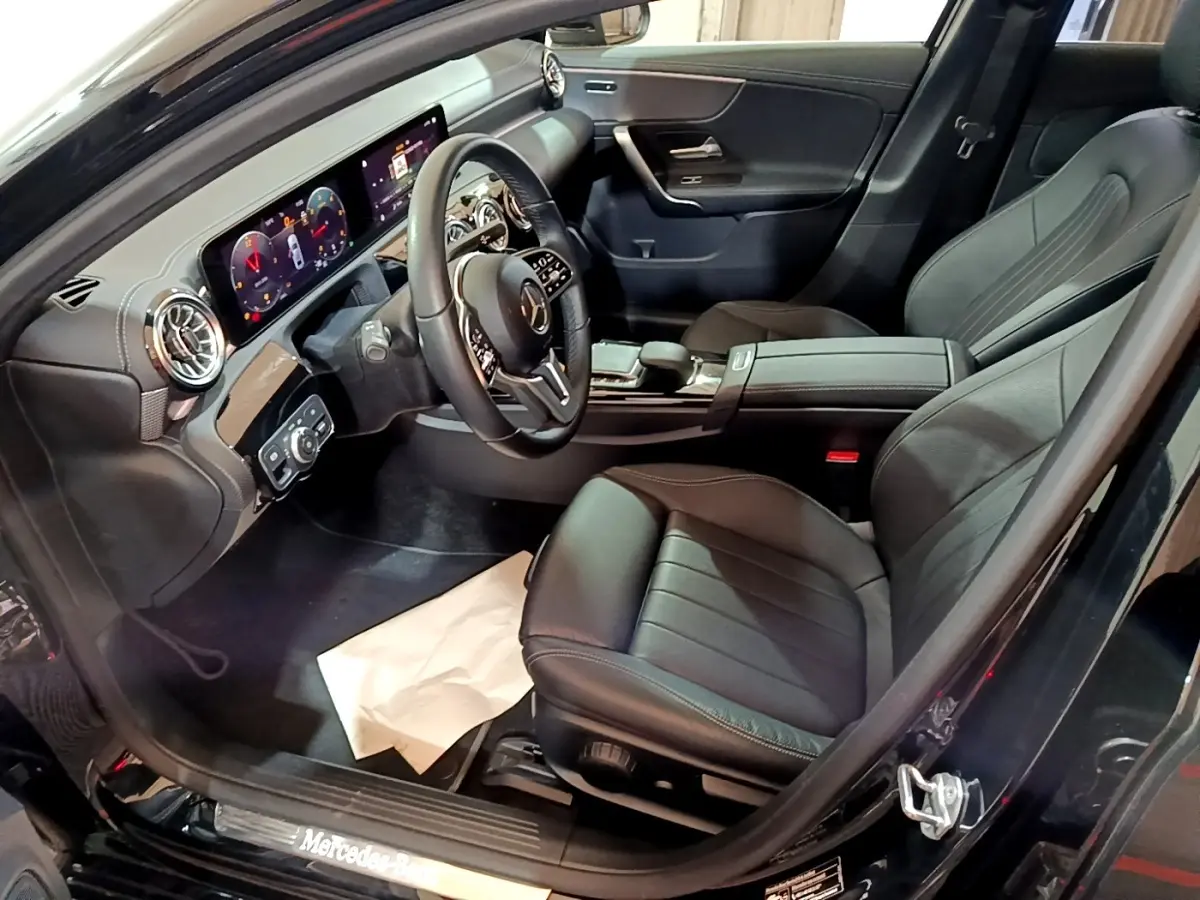 Vue intérieure côté conducteur de la Mercedes Classe A Berline noire, avec tableau de bord numérique et sièges cuir noirs.