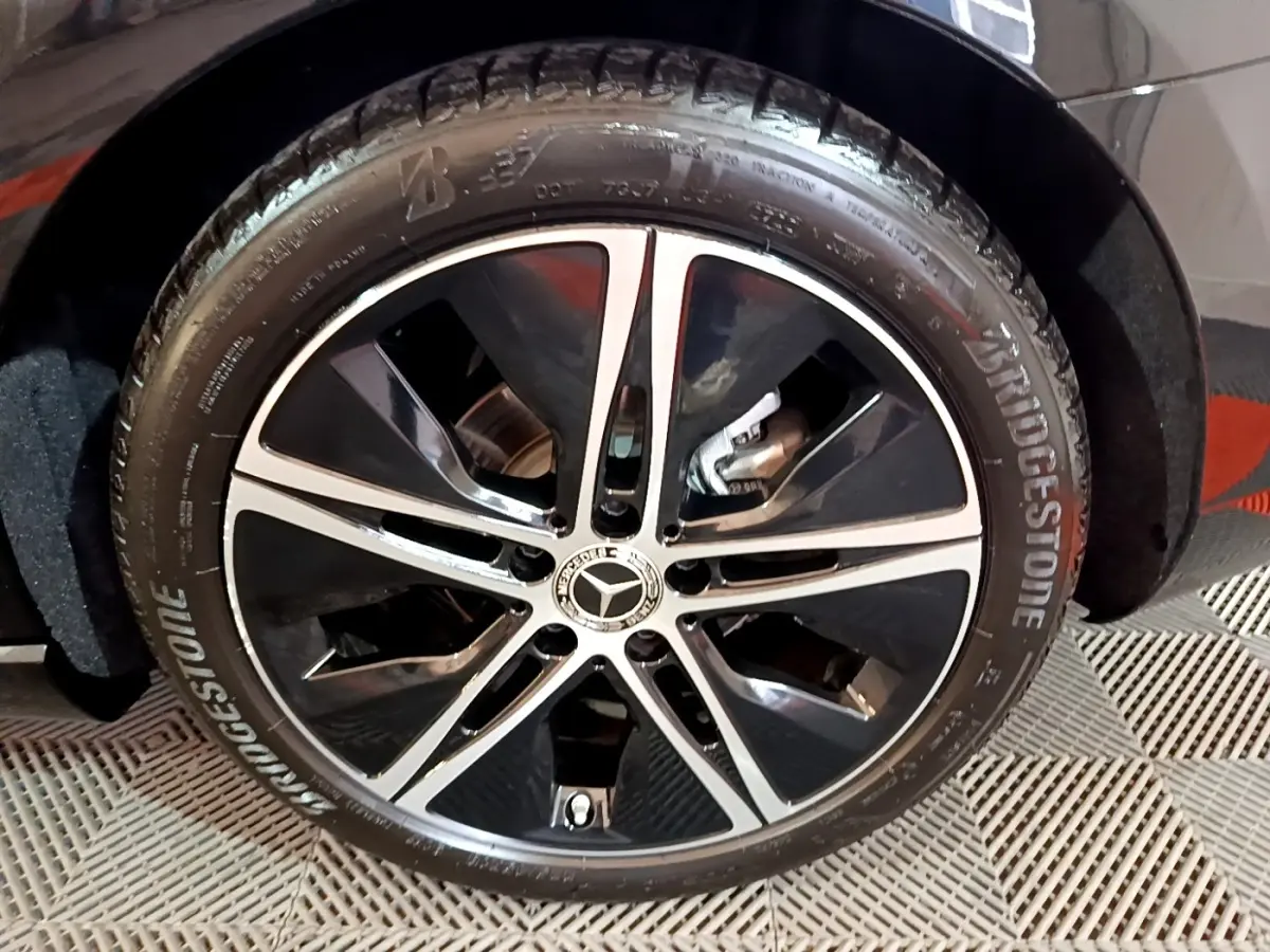 Gros plan sur la roue avant droite noire avec jante alliage bicolore et logo Mercedes visible sur une Classe A Berline noire.