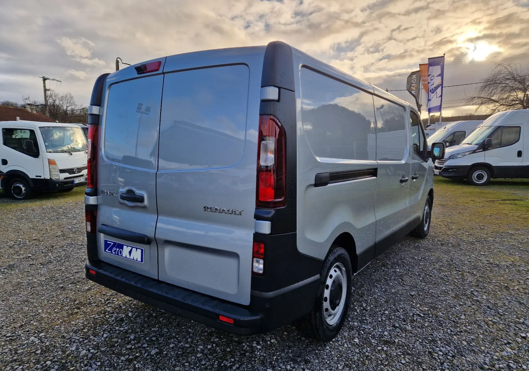 Vue 3/4 arrière droite d'un Renault Trafic Fourgon gris Highland avec portes arrière fermées sur un terrain extérieur.