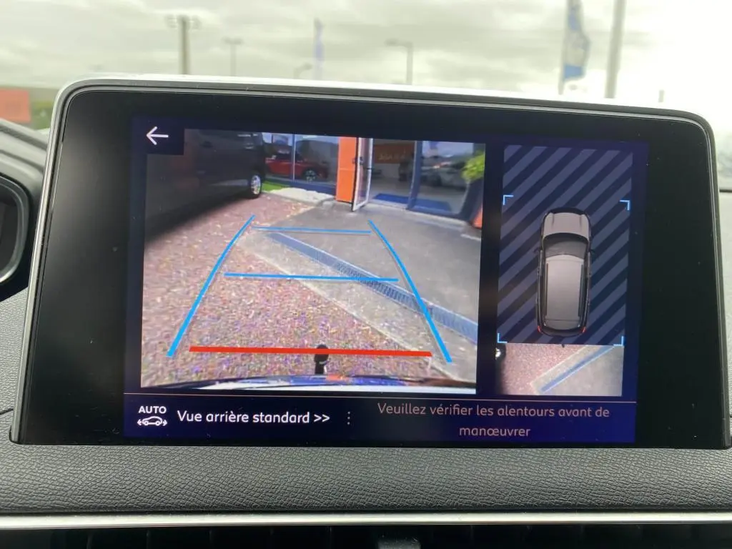 Écran tactile du Peugeot 3008 blanc montrant la caméra de recul avec vue arrière et top-down du véhicule en stationnement.