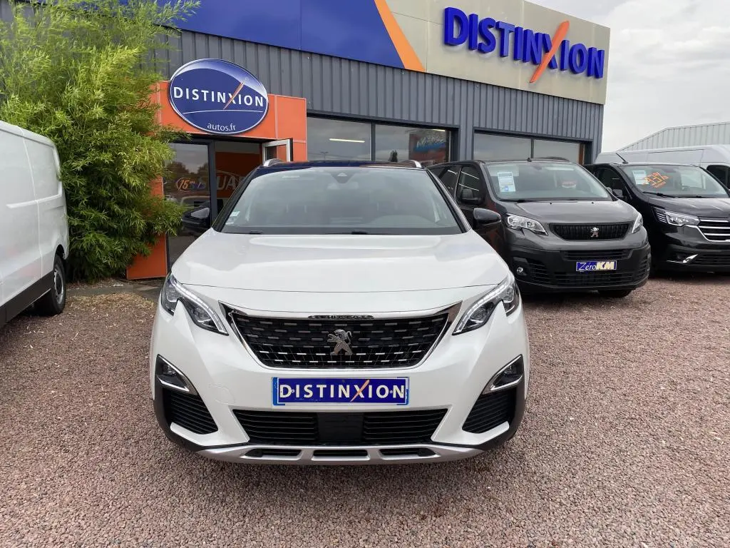 Vue frontale d'un Peugeot 3008 blanc nacré GT Line avec calandre noire et barres de toit en aluminium.