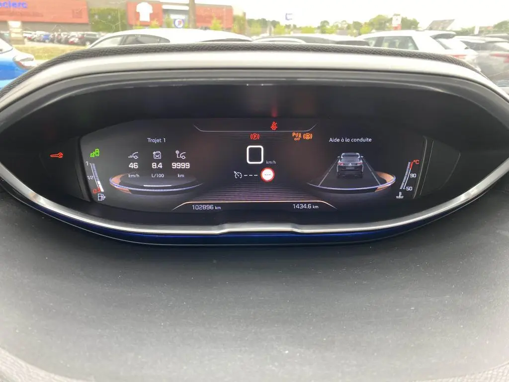 Affichage numérique du tableau de bord du Peugeot 3008 blanc, montrant l'aide à la conduite et les indicateurs de vitesse et consommation.