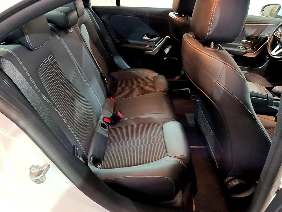 Vue intérieure côté arrière gauche de la Mercedes CLA 200 d Business Line blanche, sièges arrière en cuir noir avec surpiqûres.