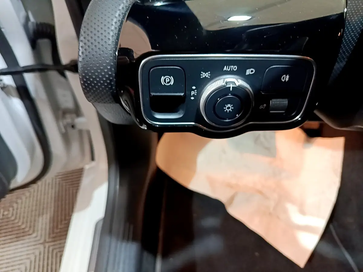 Gros plan sur le panneau de commande des phares et du frein à main électrique dans une Mercedes CLA 200 d Business Line blanche.