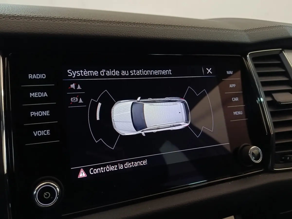 Écran tactile intérieur montrant le système d'aide au stationnement avec vue aérienne du Skoda Kodiaq blanc.
