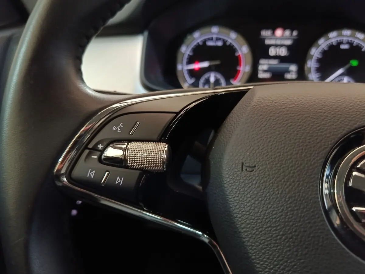 Gros plan sur la partie gauche du volant noir du Skoda Kodiaq 2022 avec commandes audio et affichage digital en arrière-plan.
