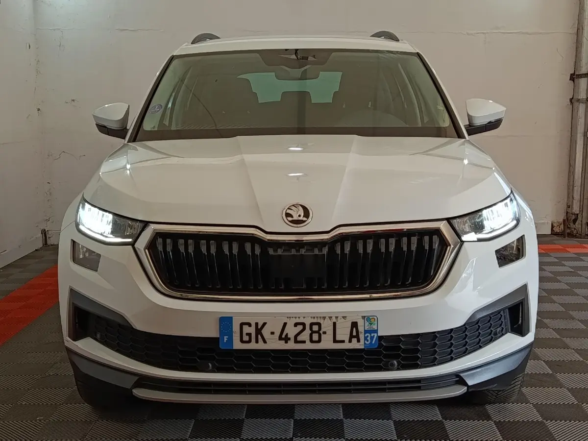 Vue frontale d'un Skoda Kodiaq blanc 2022 avec phares LED allumés et calandre noire distinctive.