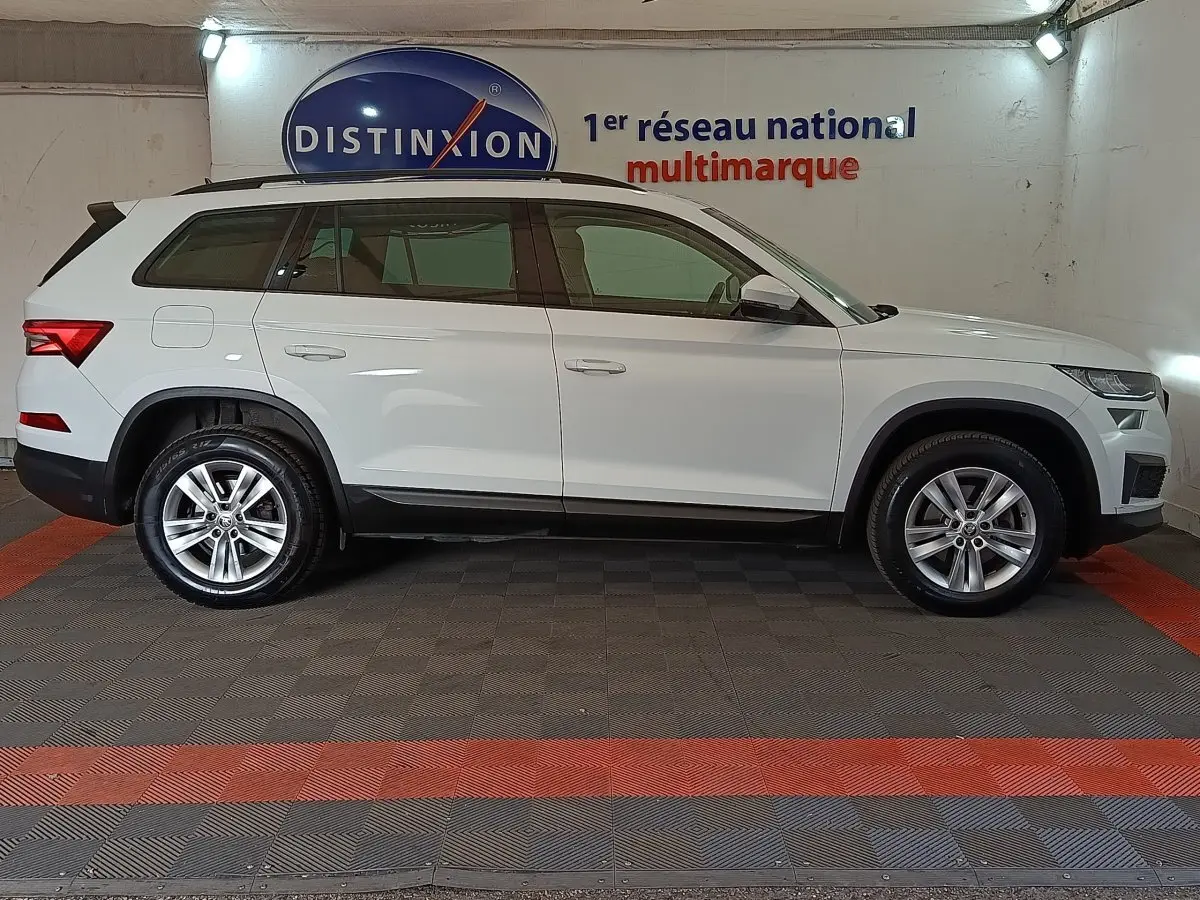 Vue de profil côté gauche d'un Skoda Kodiaq blanc 7 places, version Ambition, dans un showroom multimarque.
