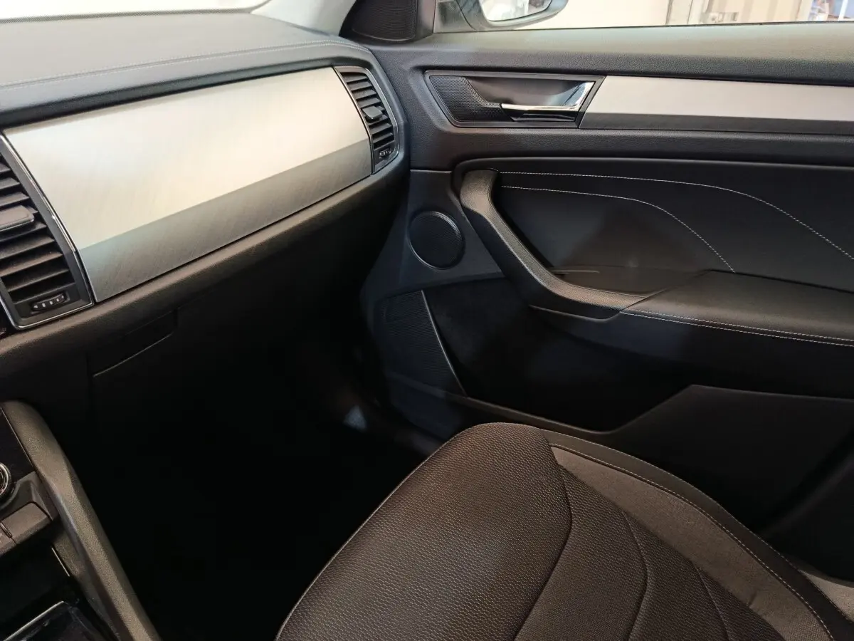 Intérieur côté passager du Skoda Kodiaq 2022, planche de bord claire et garniture noire avec surpiqûres blanches.