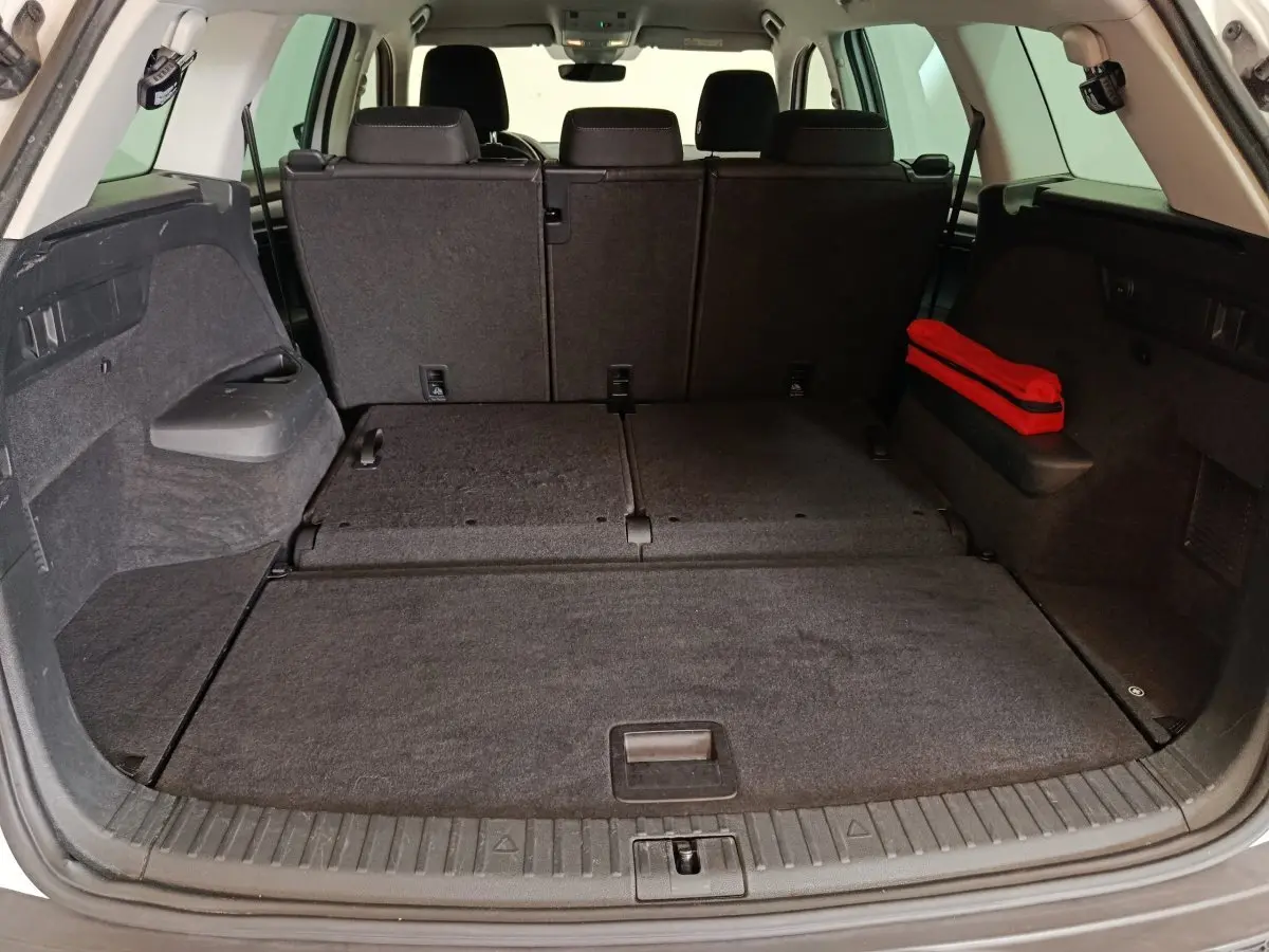Vue arrière du coffre spacieux du Skoda Kodiaq blanc 2022 avec sièges rabattus et trousse de secours rouge sur le côté droit.