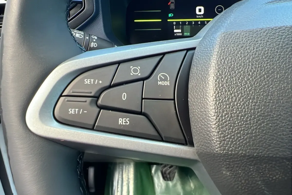 Gros plan sur les commandes au volant côté gauche du Dacia Duster blanc glacier 2025, affichage digital en arrière-plan.