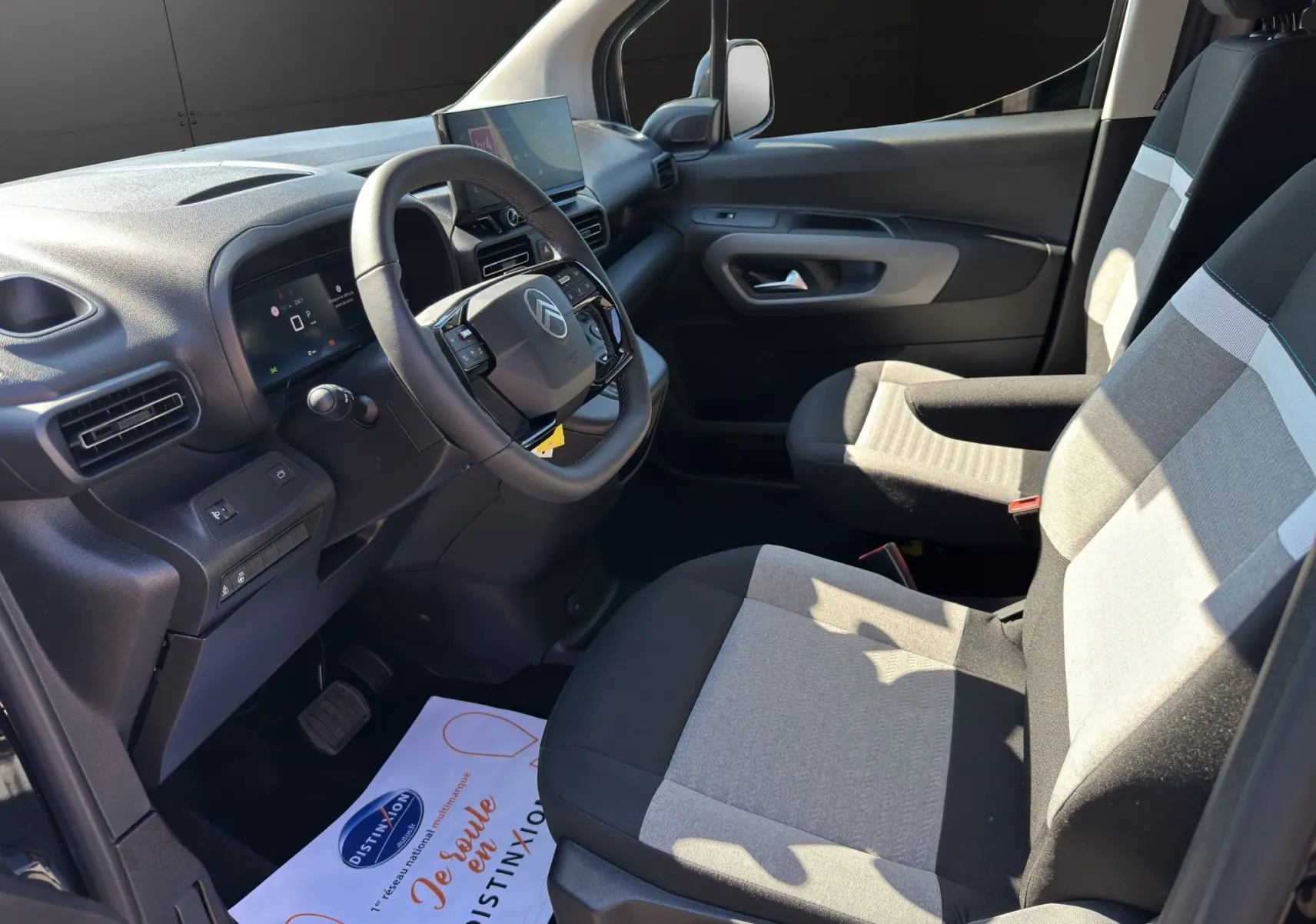 Vue intérieure côté conducteur du Citroën Berlingo 2025 noir, avec tableau de bord moderne et sièges tissu bicolore gris.