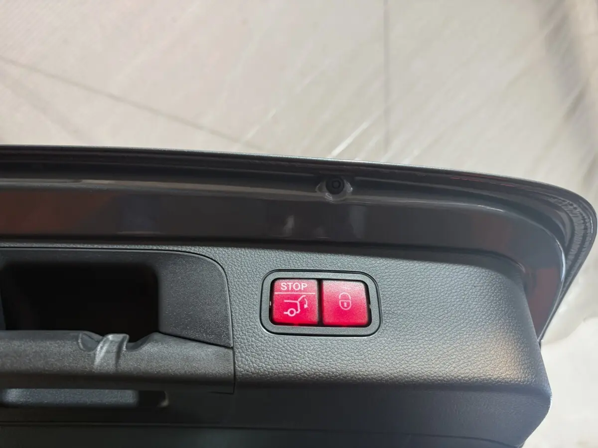 Boutons rouges d'ouverture et fermeture électrique du coffre sur le bord intérieur du hayon d'un Mercedes GLC gris foncé.