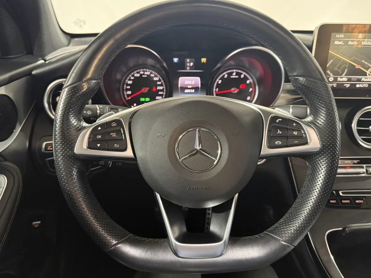 Vue rapprochée du volant cuir noir perforé de la Mercedes GLC 250 Fascination 2019 avec tableau de bord et écran multimédia.