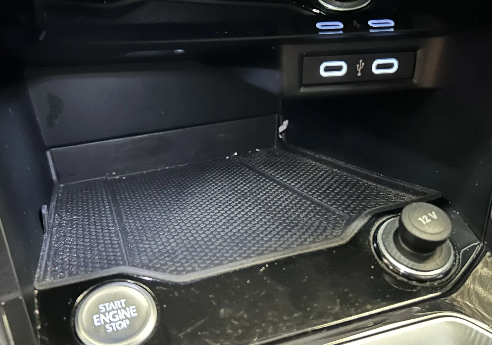 Gros plan intérieur sur la console centrale du Volkswagen T-Roc noir, montrant bouton start/stop, prise 12V et ports USB.