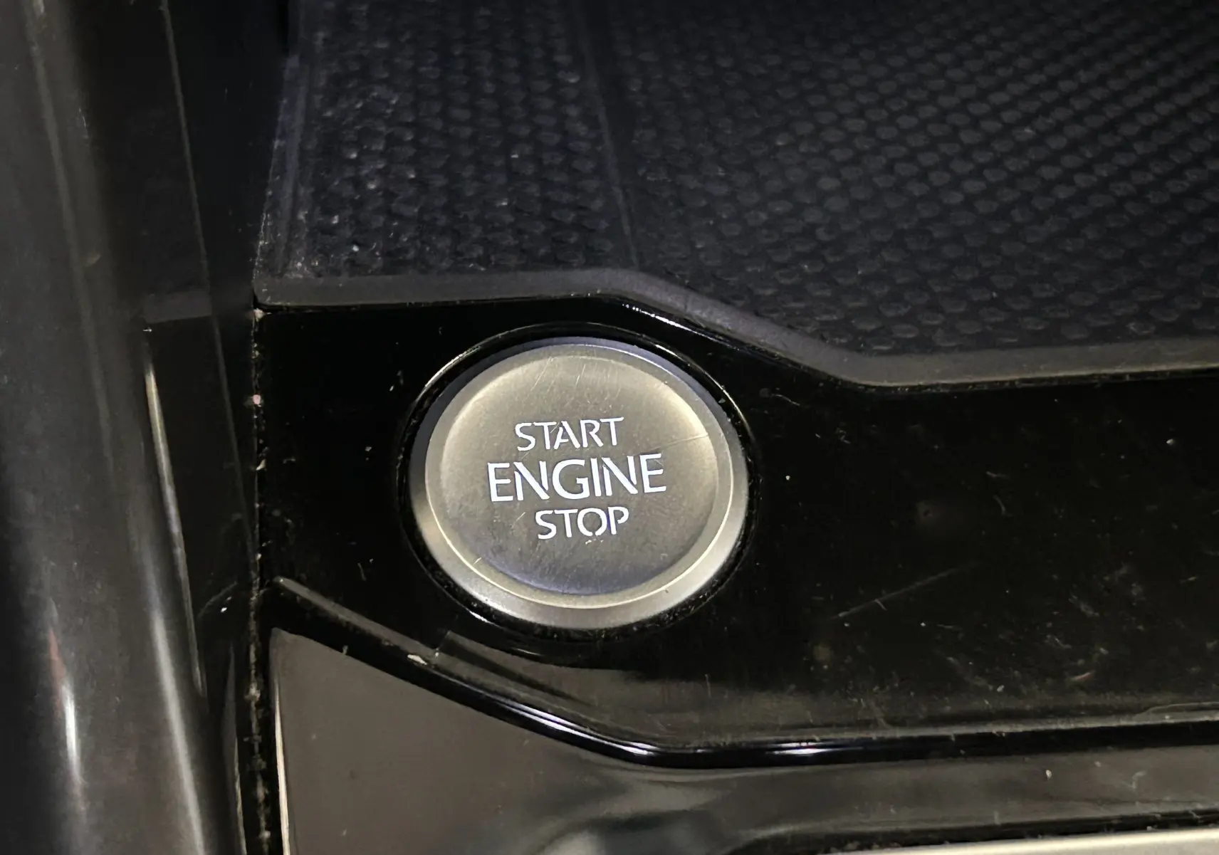 Bouton rond Start Engine Stop en gros plan sur console noire brillante d'un Volkswagen T-Roc noir.