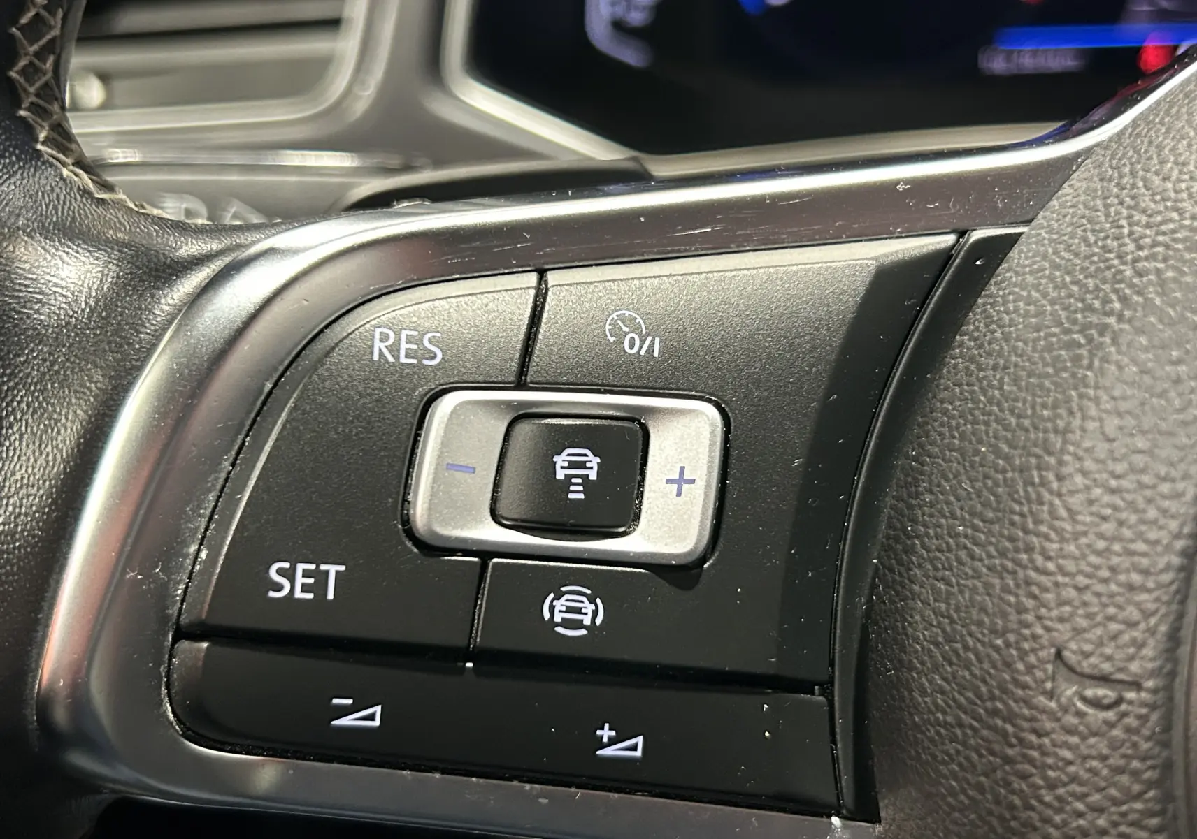 Gros plan sur les commandes noires du régulateur de vitesse au volant du Volkswagen T-Roc noir, version R-Line.