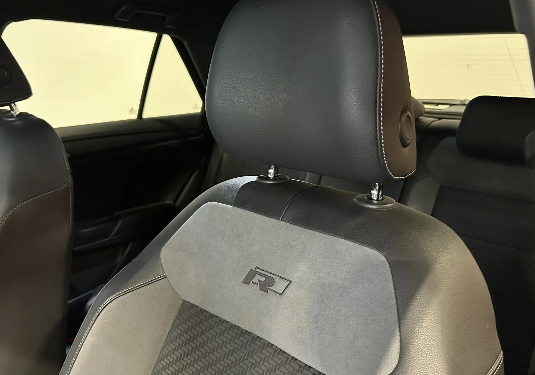 Gros plan sur le siège avant en cuir et alcantara gris avec logo R du Volkswagen T-Roc noir, intérieur arrière visible.