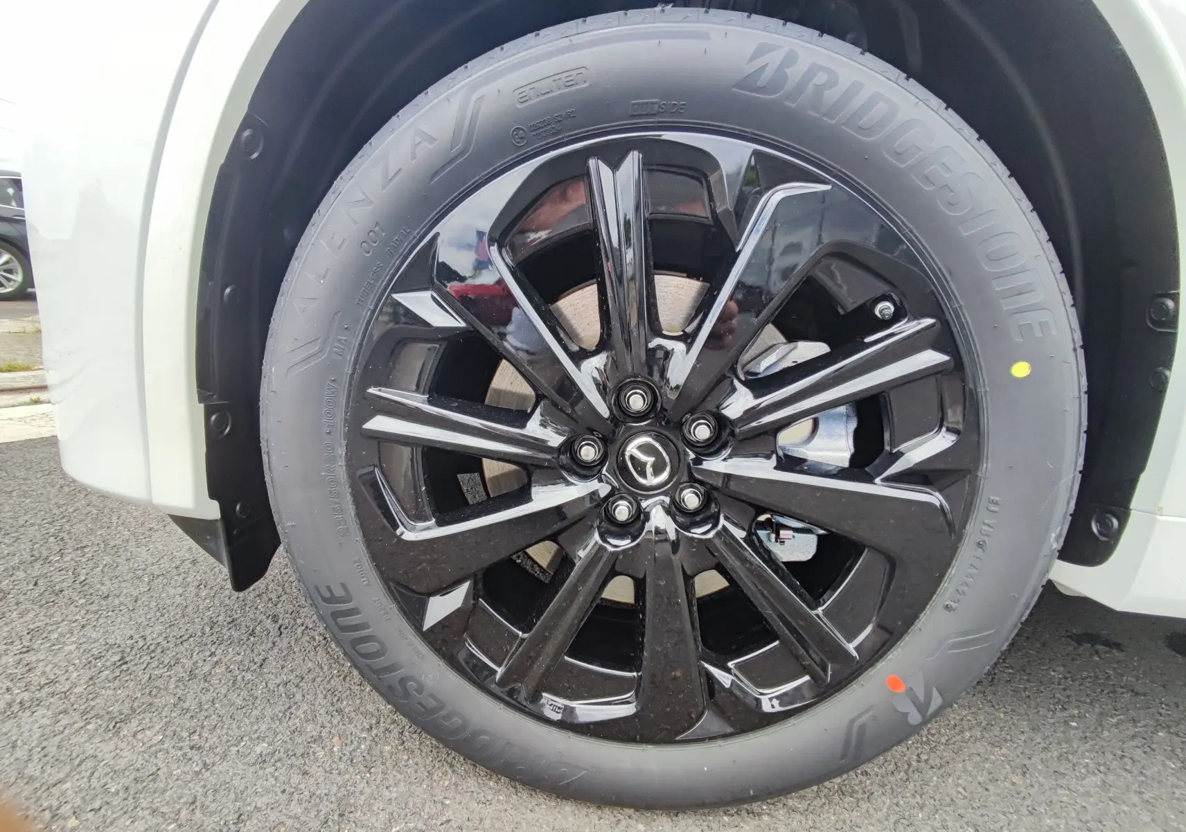 Gros plan sur la roue avant gauche d'un Mazda CX-60 blanc métal, jante noire brillante et pneu Bridgestone.