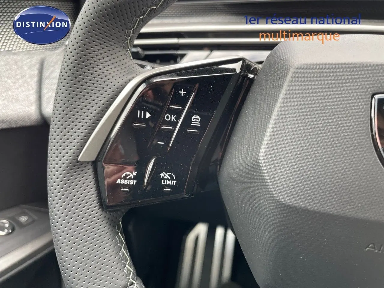 Gros plan sur les commandes du volant perforé côté gauche du Peugeot 5008 Hybrid blanc Okenite 2025.